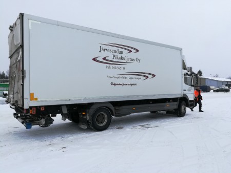 Järviseudun Pikakuljetus Oy:n kuorma-auto lumisella pihalla, kyljessä yrityksen teksti ja puhelinnumero