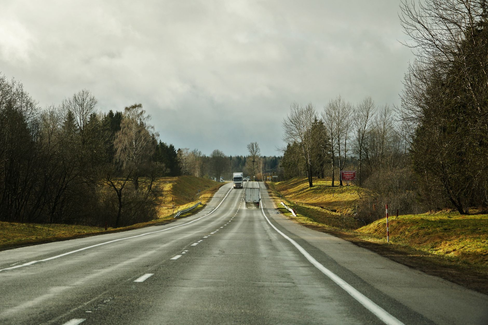 Kuvituskuva: pilvisen sään valtatie metsän halki, kaukana kuorma-autoja.